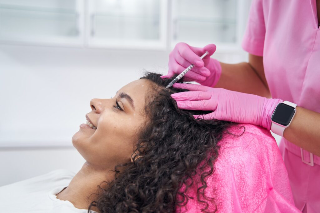 Cosmetologist performs mesotherapy procedure on the scalp of a patient